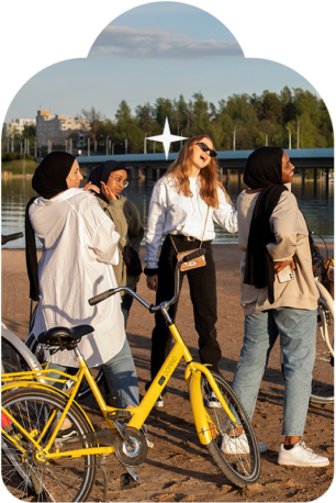 Neljä tyttöä viettää kesäpäivää hiekkarannalla. Etualalla keltainen polkupyörä.